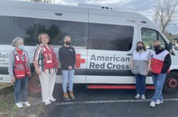 Peace Winds staff member and four Red Cross volunteers smile at the camera standing next to an American Red Cross emergency response van