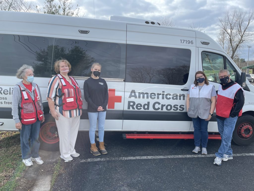 Four Red Cross volunteers and one Peace Winds employee stand in front of a large American Red Cross emergency response van