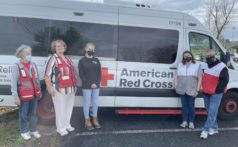 Four Red Cross volunteers and one Peace Winds employee stand in front of a large American Red Cross emergency response van