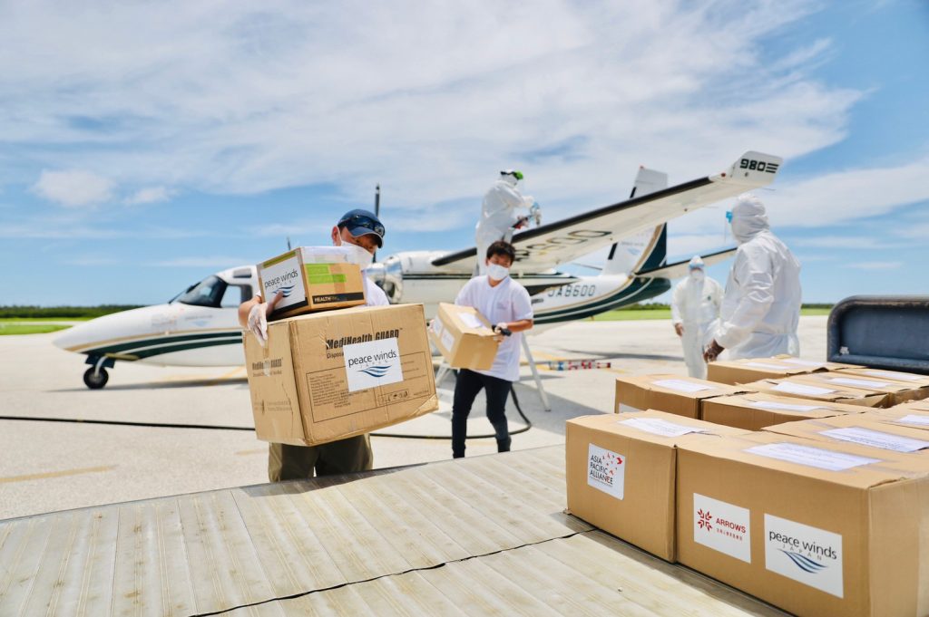 A group of Peace Winds employees unloads cardboard boxes from a small search-and-rescue plane