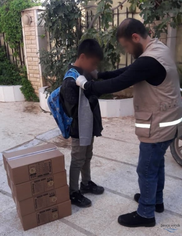 A Peace Winds worker wearing a tan vest helps an older boy try on a winter jacket