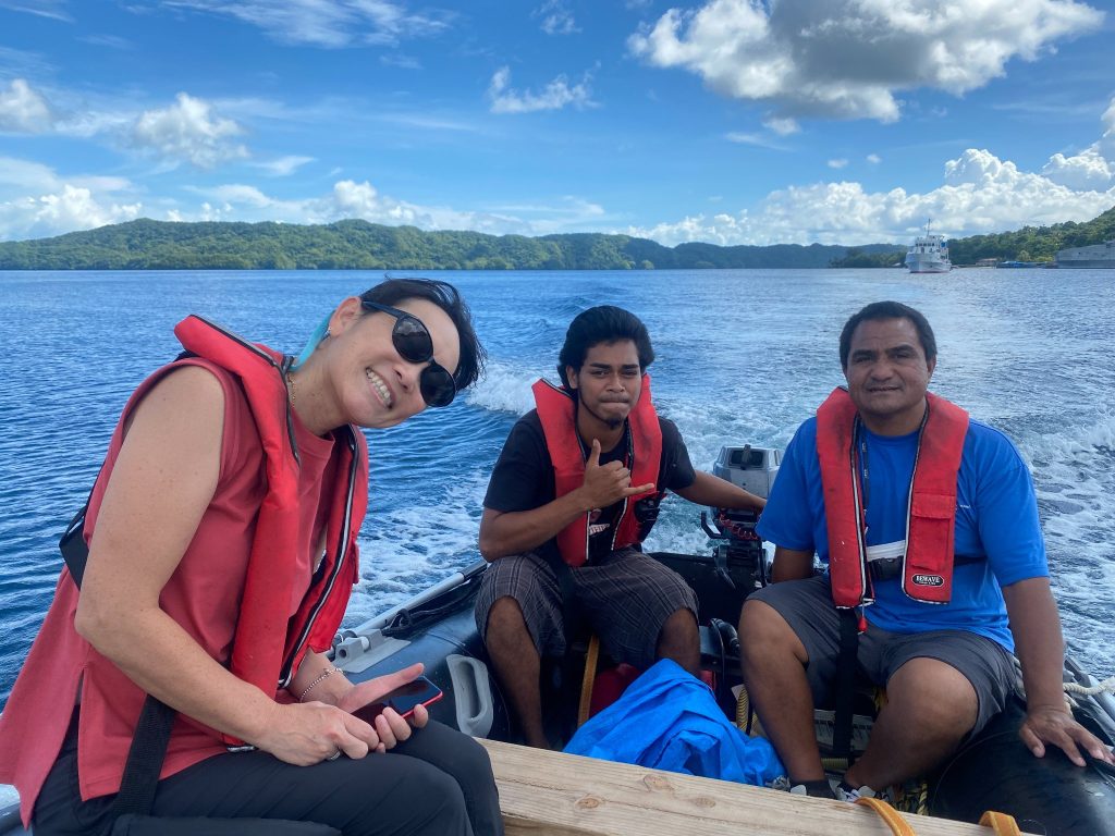 Three Peace Winds Palau staff members sit in a small boat with blue water and a blue sky in the background