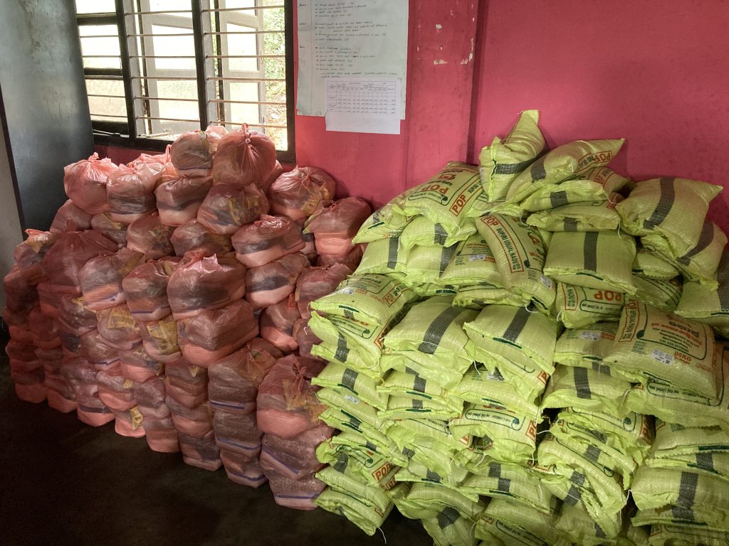 Hundreds of pink and yellow bags of nonperishable food are stacked several feet high against a pink wall
