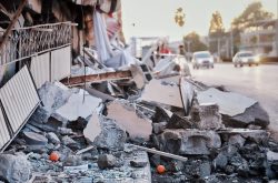 Rubble of a destroyed building with two oranges covered in dust. A street with two cars is blurred in the background