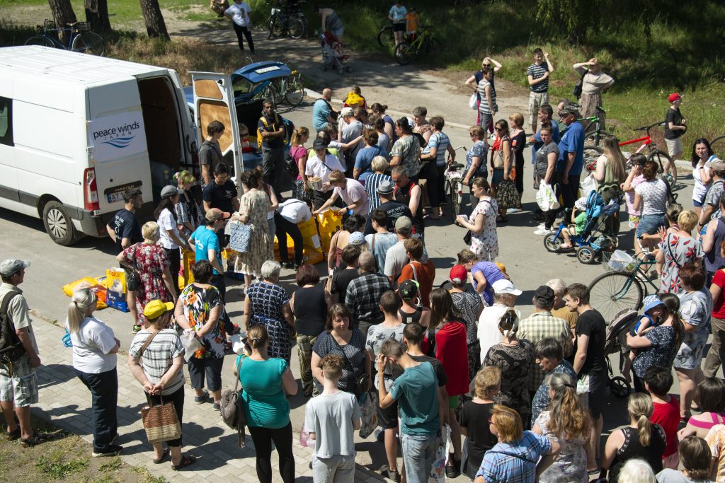 aerial view of dozens of Ukrainian people standing around a white "Peace Winds" branded van