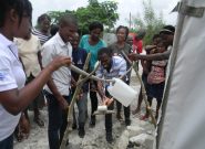 A group of Haitian adults watched a Peace Winds worker demonstrate how to use an outdoor hand-washing station