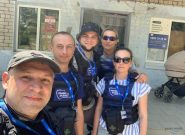 Five Ukrainian workers wearing blue and black vests smile for a selfie
