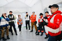 Team of 8 Peace Winds/ARROWS staff members stand inside a white tent wearing red or blue emergency response uniforms