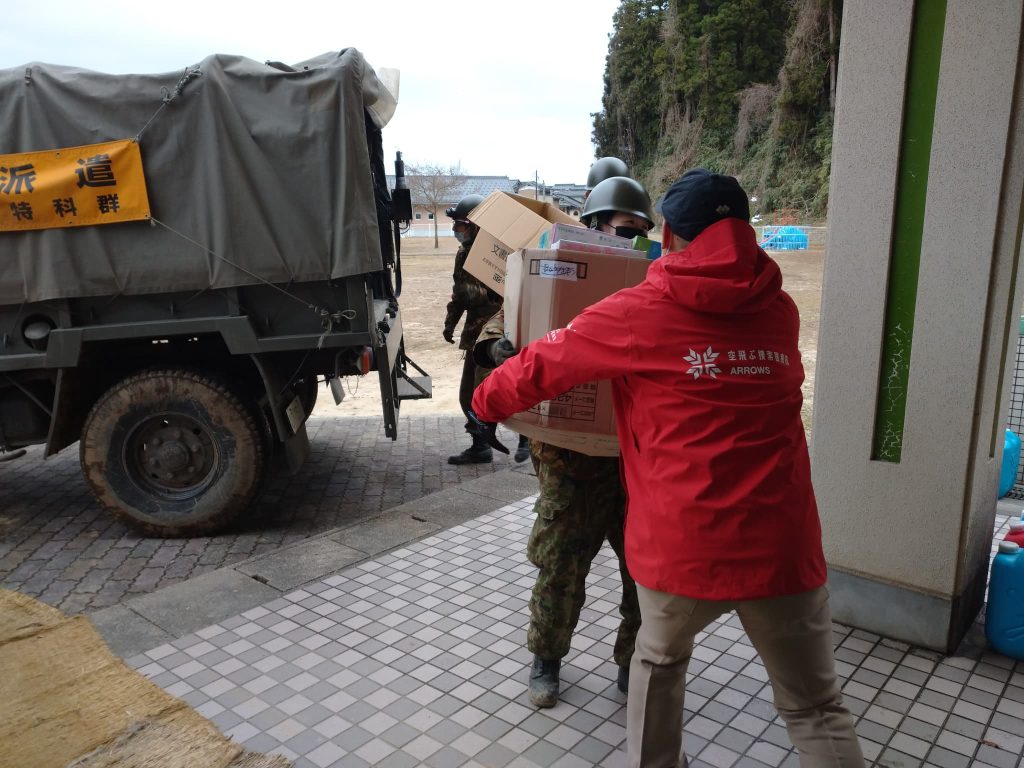 Person in a black long sleeve passes a cardboard box to a Peace Winds staff member wearing a red jacket