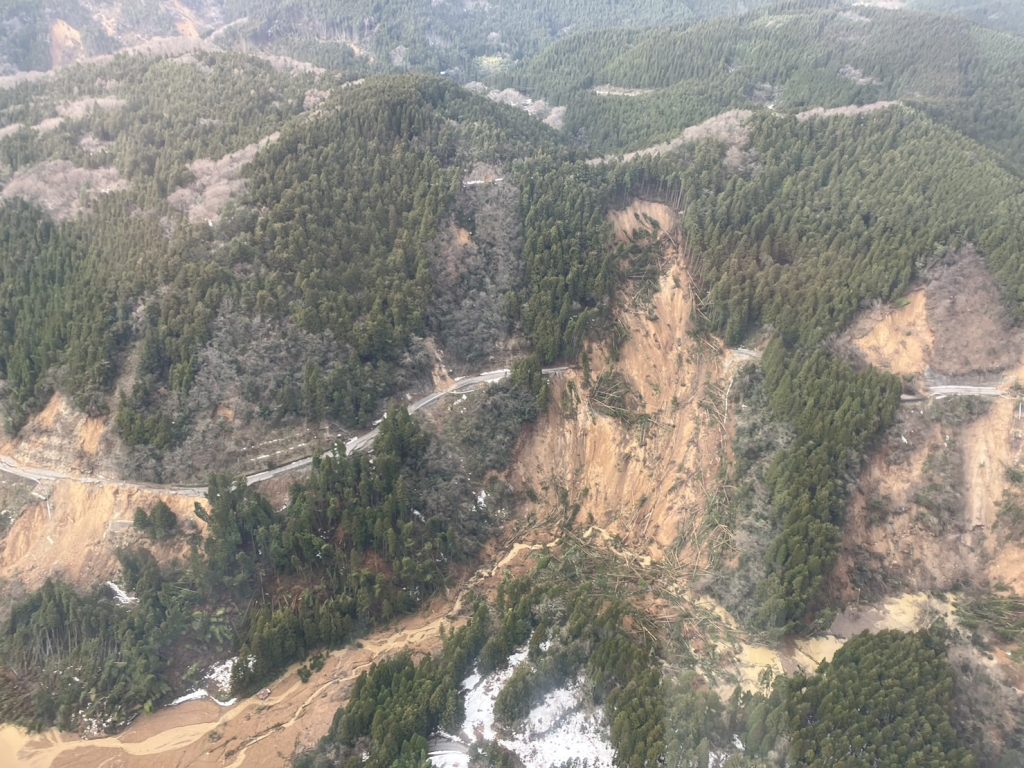 Bird's-eye view of a muddy landslide and trees covering a mountain road