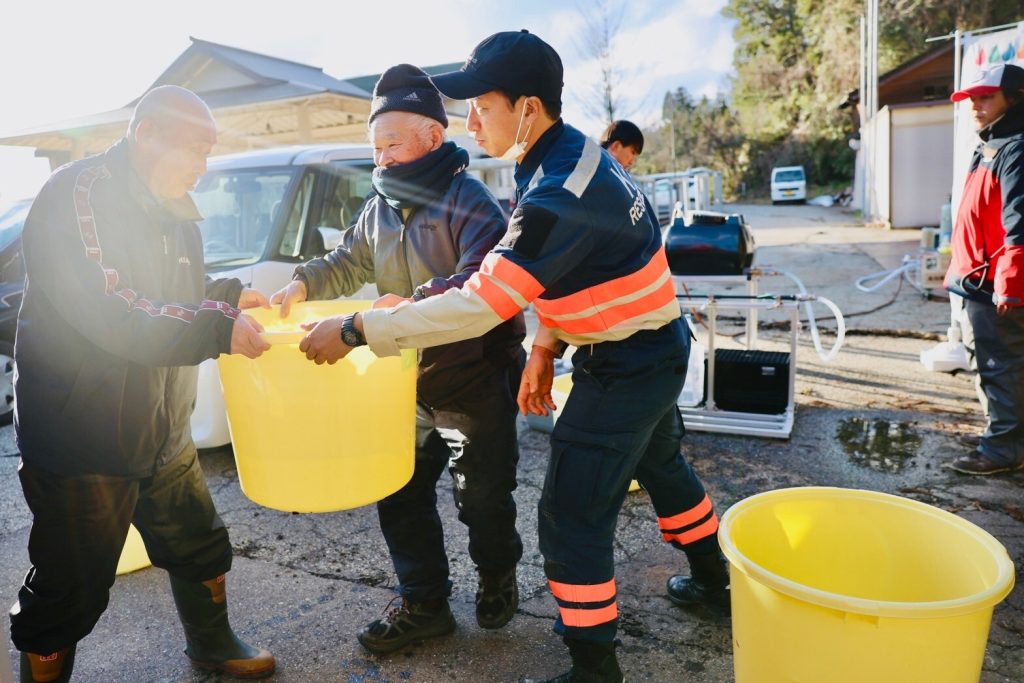 Rescue workers pass a yellow bucket of water to a man wearing black clothing