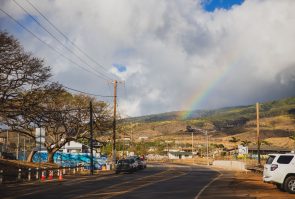 View of a town from a road with clouds and a rainbow overhead