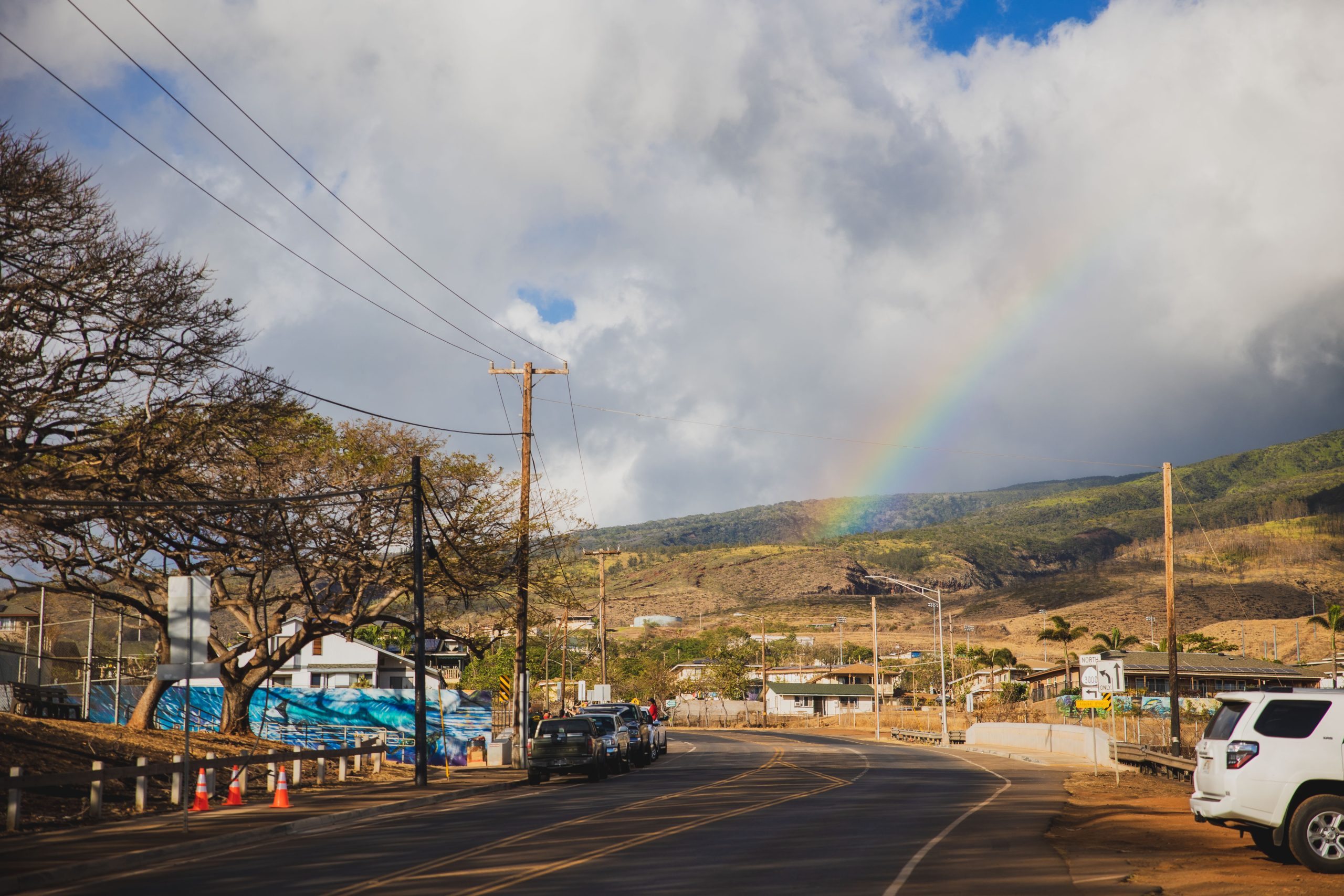 View of a town from a road with clouds and a rainbow overhead