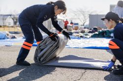 Two women in ARROWS uniforms unroll a plastic tent