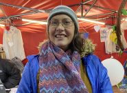 Smiling woman wears a blue coat and a knit scarf with blue and purple stripes of color