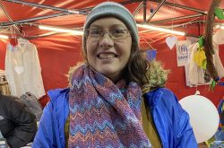 Smiling woman wears a blue coat and a knit scarf with blue and purple stripes of color