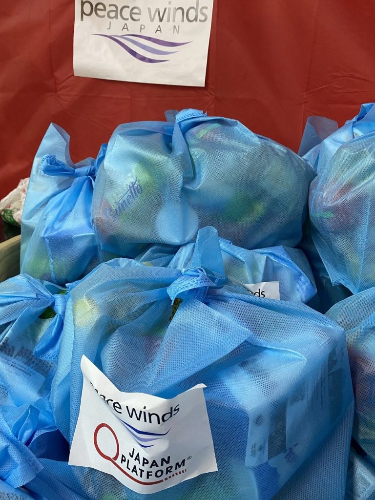 pile of food kits wrapped in blue fabric bags with Peace Winds and Japan Platform logos