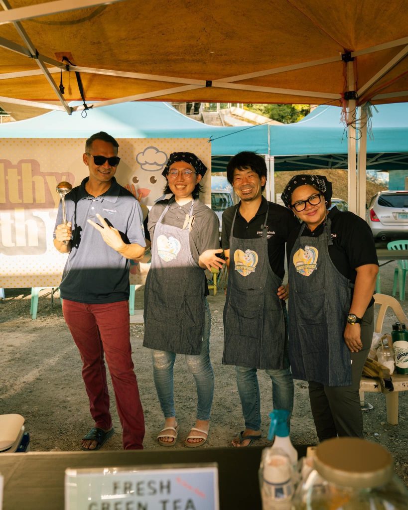 4 people in dark blue aprons with a blue and yellow kensing logo smile while standing under a tent