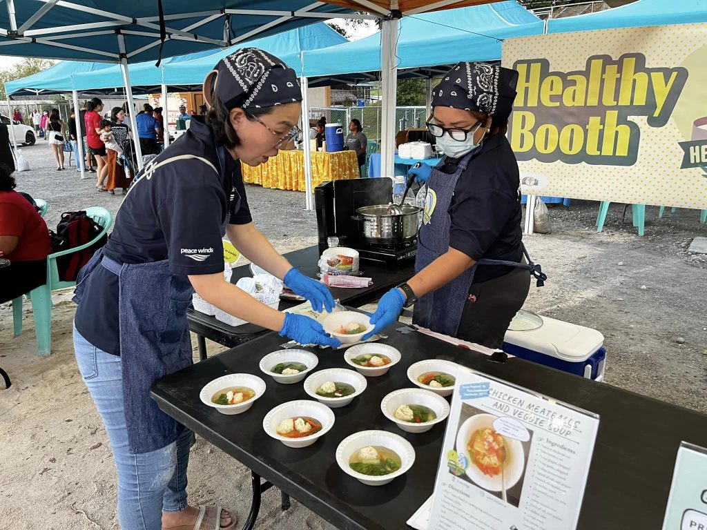 two peace winds staff members arrange bowls of soup on a table at a market booth