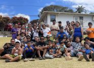 Large group of children and adults in colorful clothing stands and sits outside while smiling for the photo