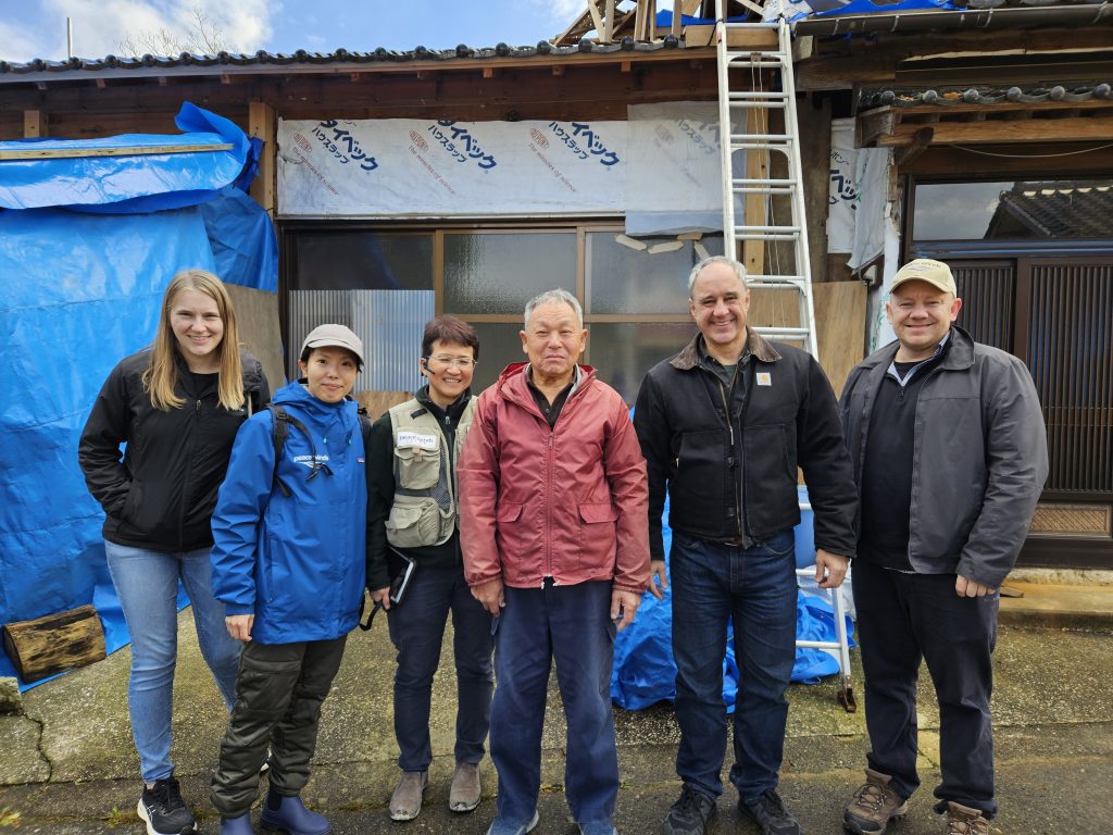 Group of 3 women and 3 men standing together in front of a house under renovation