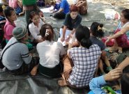 A group of Burmese women sits on a tarp on the ground