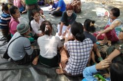 A group of Burmese women sits on a tarp on the ground