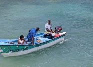 two Haitian men and one woman are in a small teal and white fishing boat surrounded by a clear blue ocean