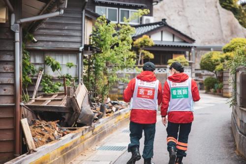 two people wearing ARROWS vests/uniforms walk away from the camera on a sidewalk in japan